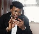 A cheerful man wearing a stylish outfit uses a smartphone while seated in a modern indoor setting.